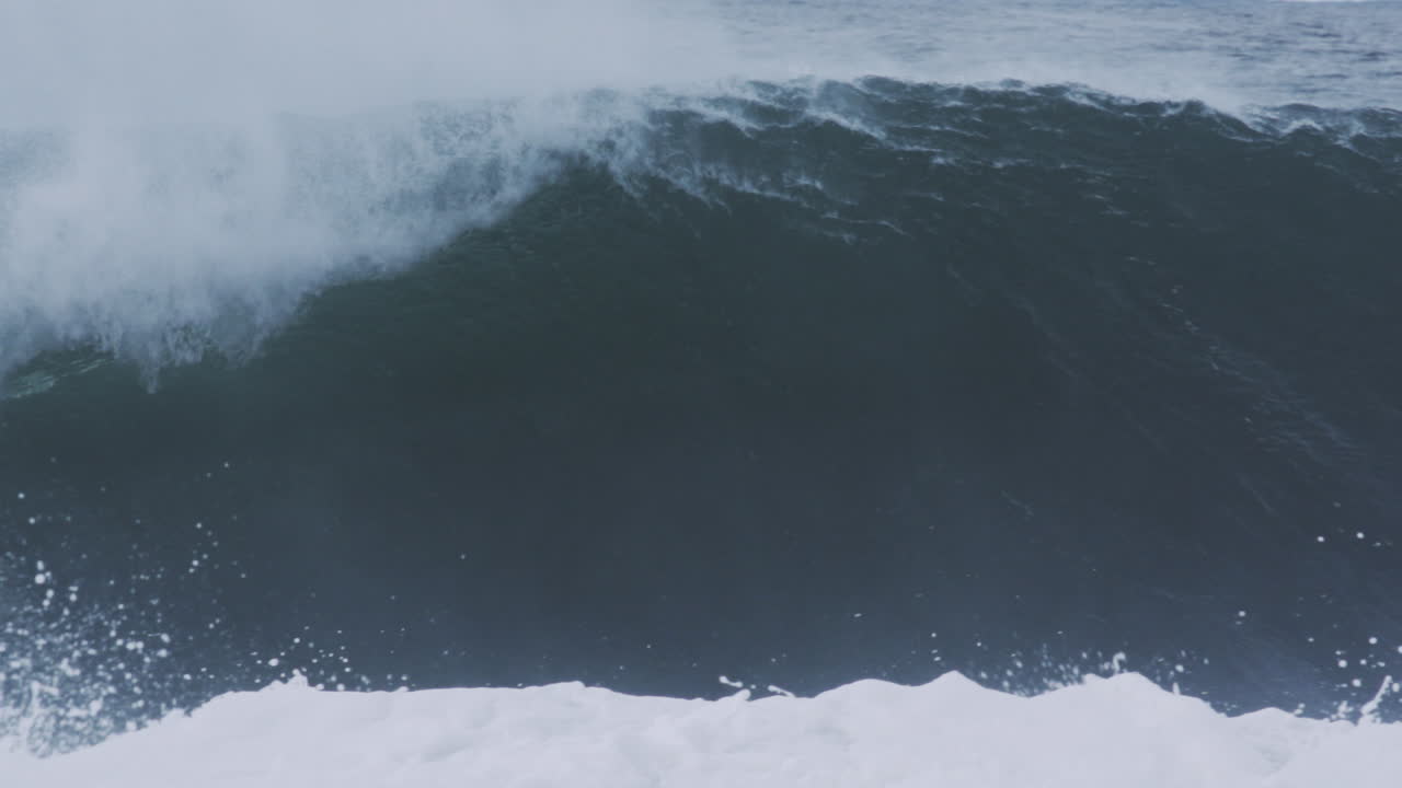 Curling lip of blue wave spits mist and water outward, framed in slow motion telephoto view