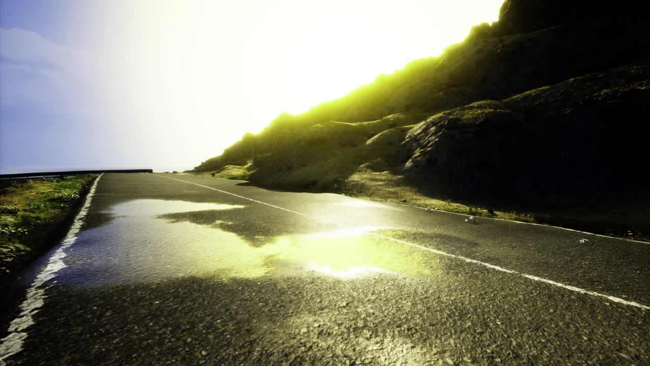Scenic road with sunlight shining over wet pavement near mountains