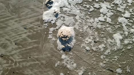 Dirty-sea-foam-froth-slowly-moving-across-sandy-Anglesey-beach-with-tide-waves