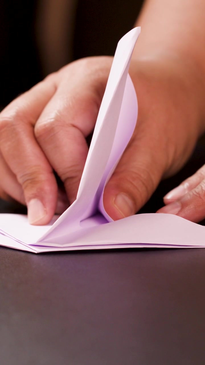 Adult hands carefully fold light paper into an origami boat, close-up, warm indoor lighting