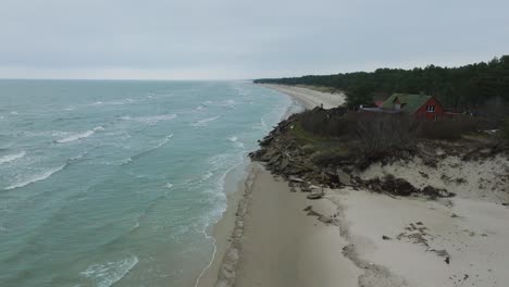 Aerial-establishing-view-of-Baltic-sea-coast-on-a-overcast-winter-day,-a-house-at-the-beach-with-white-sand,-coastal-erosion,-climate-changes,-wide-drone-shot-moving-forward,-camera-tilt-down