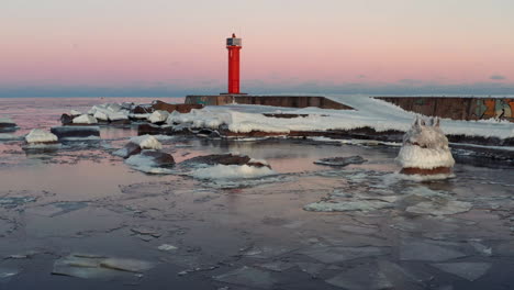 icy breakwater and lighthouse at sunset coastline, panning drone shot