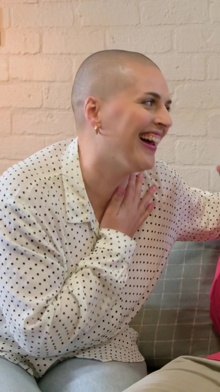 Video verticale: Donna sorridente con camicetta a pois che risponde a un commento del partner sul divano, mentre l'uomo ride.