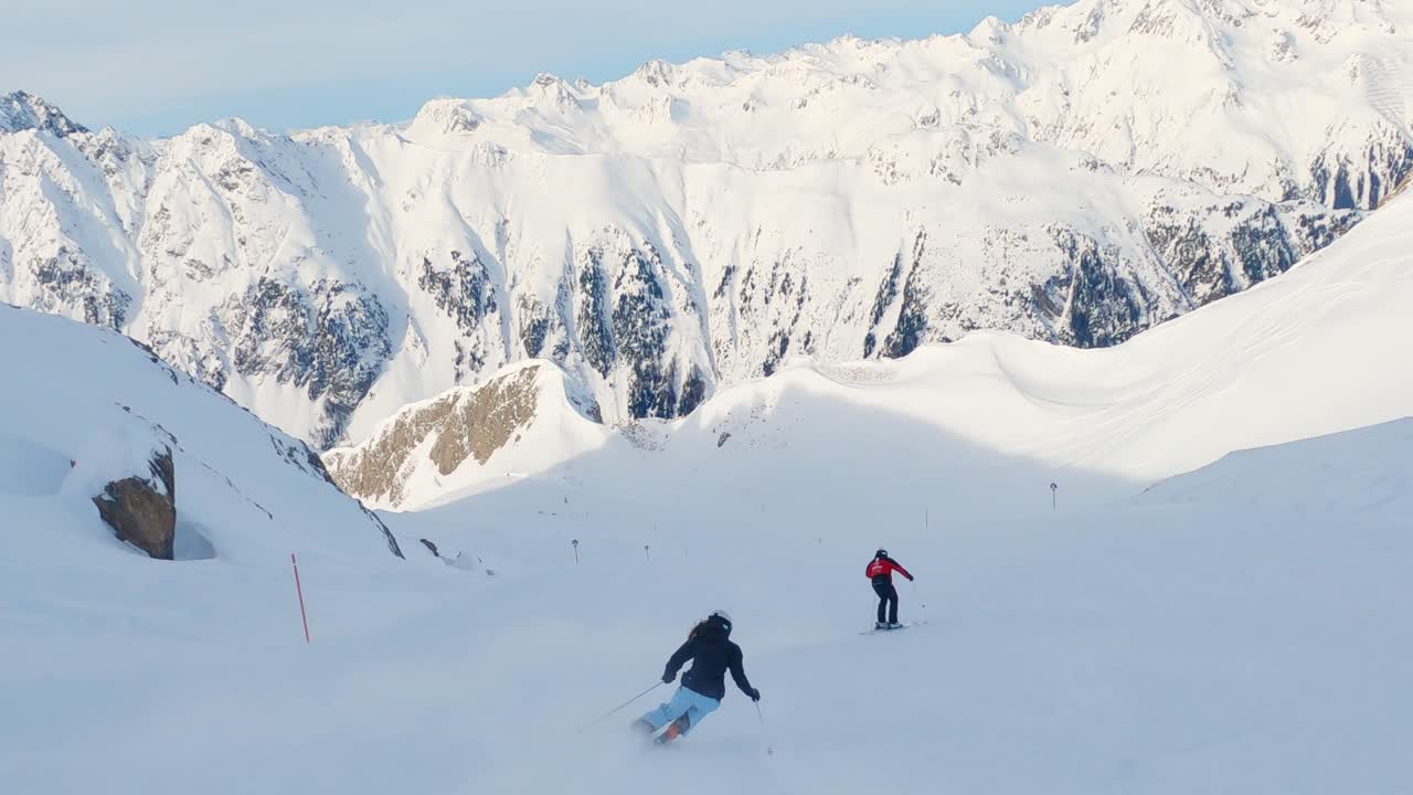 Sci sportivo con ottima tecnica sciistica, coppia di sciatori professionisti che esegue lunghe curve con una splendida vista invernale. Cielo blu, neve fresca e polverosa, capelli lunghi ed equipaggiamento da sci moderno, telecamera a 4k che segue.