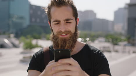 retrato en cámara lenta de un apuesto joven hombre hipster estudiante con barba disfrutando de mensajes de texto navegando usando una aplicación de redes sociales de teléfono inteligente en un fondo urbano