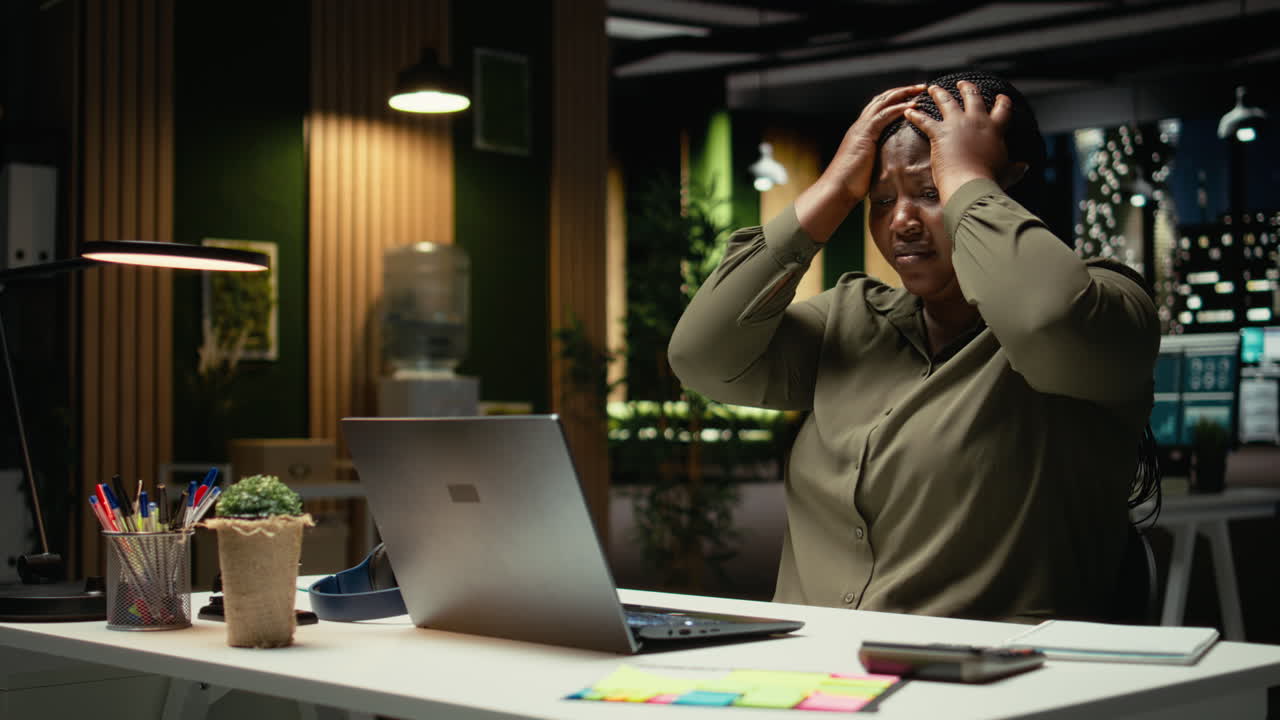 Black businesswoman distressed and burdened at the office after hours