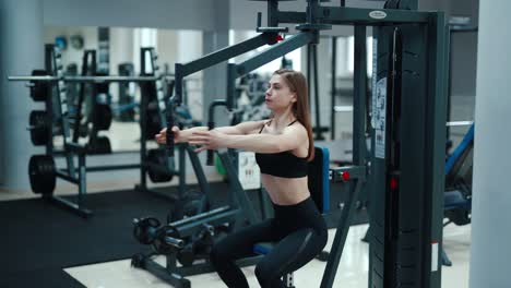sports girl in a black top and leggings performs an exercise on his chest simulator in a fitness club. blurred background