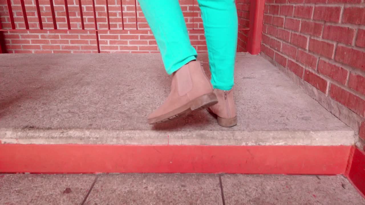 Person walking up concrete step, wearing turquoise pants and beige suede shoes