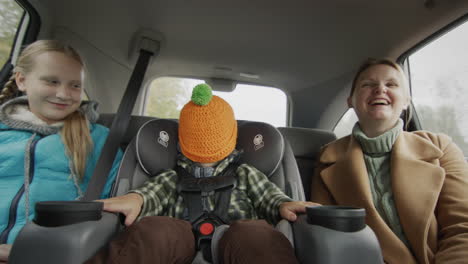 a cheerful company led by a two-year-old baby in a child car seat travels in a car