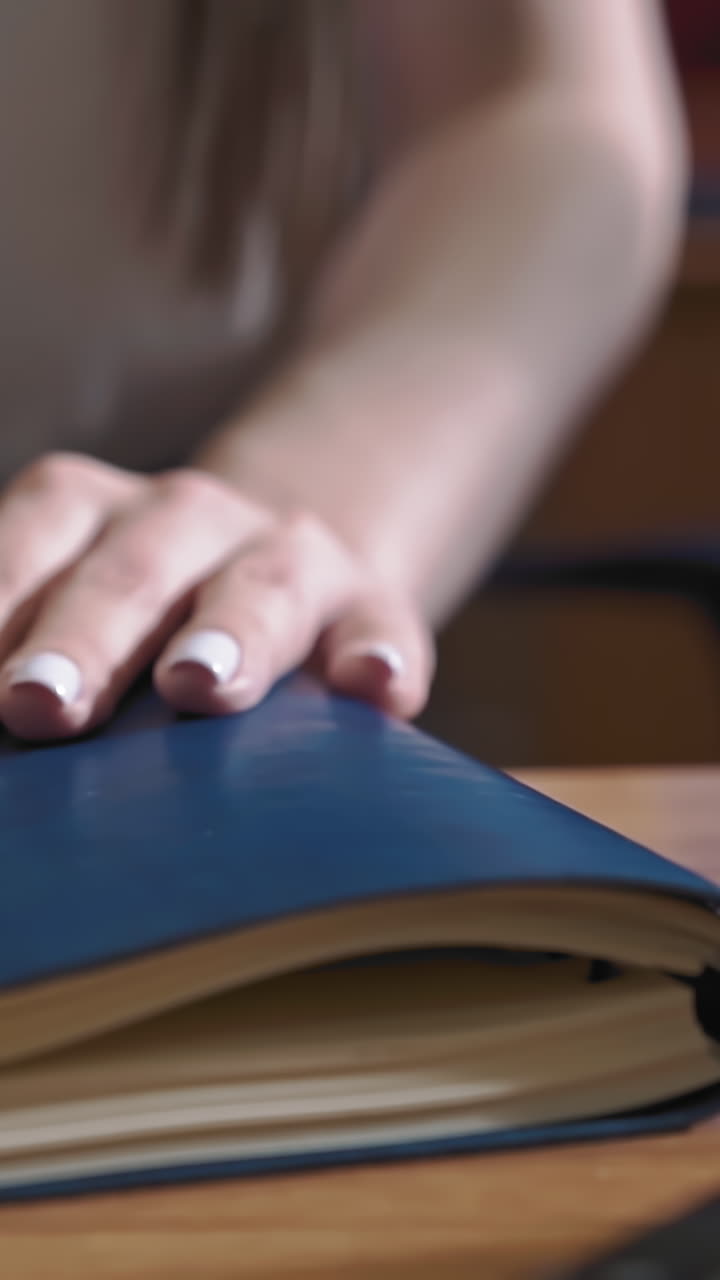 Young long haired businesswoman in light blouse sits down at table and opens paper notebook with pen in light office closeup slow motion