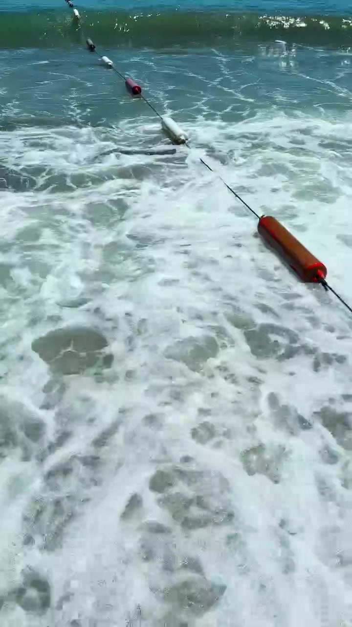 En boj som flyter i havsvågor nära en sandstrand under en klar solig dag