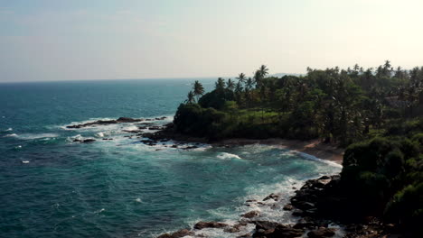 drone flies sideways over ocean waves crashing into a rocky coast during sunset near silent beach, sri lanka.