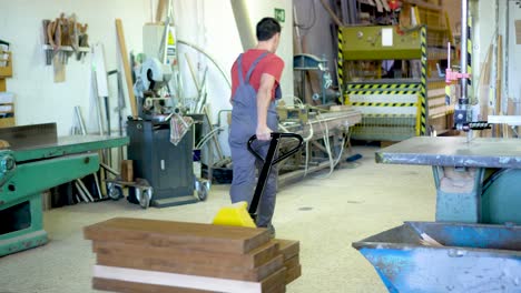 a worker moving wood with a pallet jack in a woodworking workshop