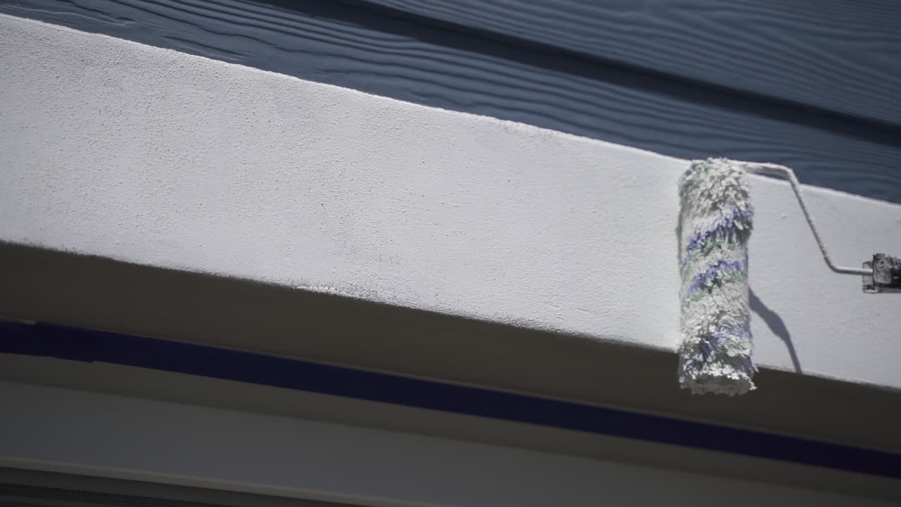 Slow motion shot person painting window frame of house with paint roller during sunny day
