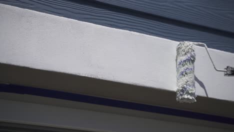 slow motion shot person painting window frame of house with paint roller during sunny day