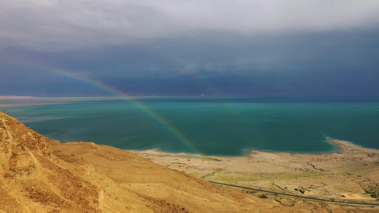 volar al arco iris frente a la vista del mar muerto, primer plano del acantilado del desierto, toma aérea