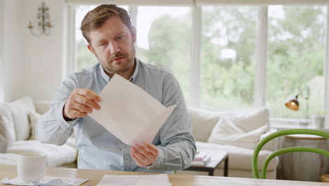 hombre sonriente sentado en la mesa en casa revisando las finanzas domésticas carta de apertura con buenas noticias
