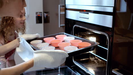 Close-up-of-mother-and-daughter-are-putting-cakes-in-the-oven