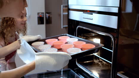 close up of mother and daughter are putting cakes in the oven