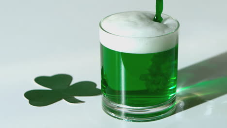 Green beer pouring into a tumbler beside paper shamrock