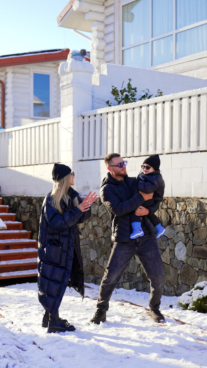 Modern fashionable Caucasian parents wearing warm clothes stand outdoors. Loving couple entertain their little baby boy. Vertical video.