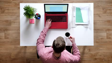 young man in glasses working and typing on laptop, women giving him coffee, topshot, sitting behind table