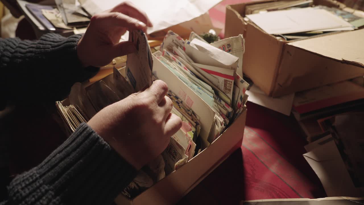 A person&rsquo;s hands going through a box of old letters and postcards stacked haphazardly in a box