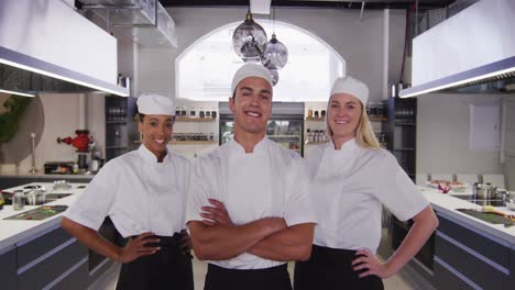 chefs multiétnicos vistiendo chefs blancos en la cocina de un restaurante mirando a la cámara y sonriendo