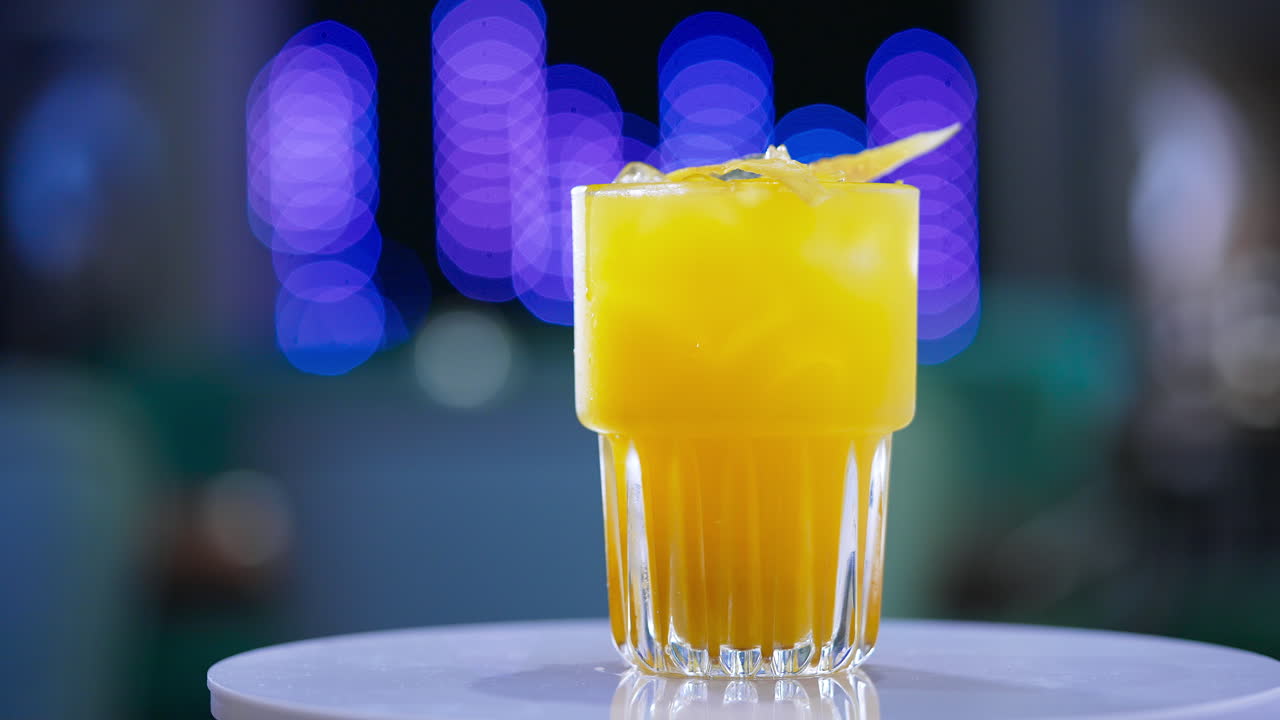 A glass filled to the top with beverage of yellow color. Savory cocktail on the rotating table close up. Blurred backdrop.