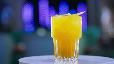 a glass filled to the top with beverage of yellow color. savory cocktail on the rotating table close up. blurred backdrop.