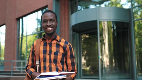 african american man smiling at the camera while preparing to exams during the break near the college