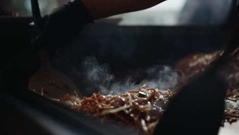 Revolviendo-Fideos-Fritos-Humeantes-Con-Espátulas-De-Metal-En-La-Parrilla-Del-Festival