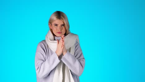 young blonde woman feeling cold, shivering, blowing in her hands to warm up, colorful studio shot