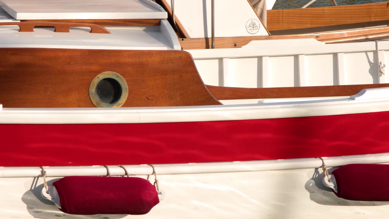 Primo piano dello scafo di una barca in legno vintage con parabordi rossi che galleggia in acqua calma