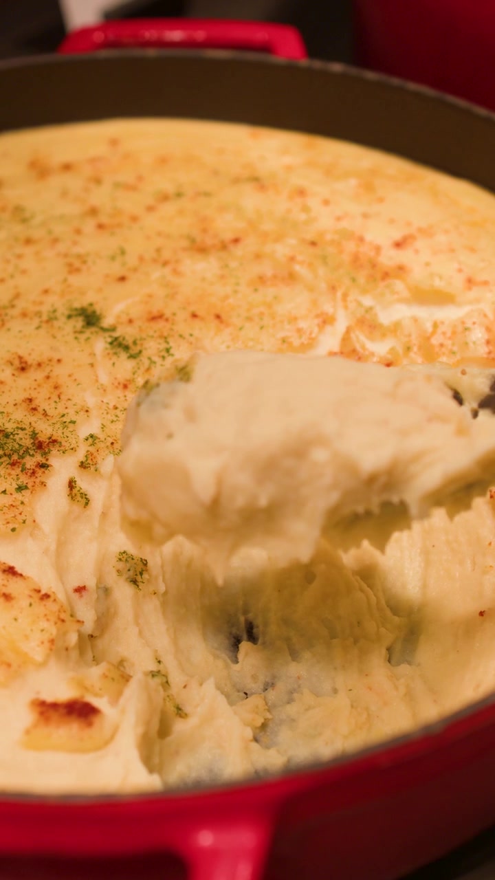 Un cucchiaio da portata raccoglie purè di patate cremoso condito con paprika da una pentola da buffet rossa