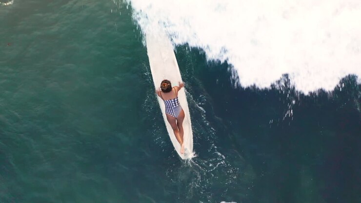 Aerial Shot Of Female Surfer Paddling A Wave On A Surfboard