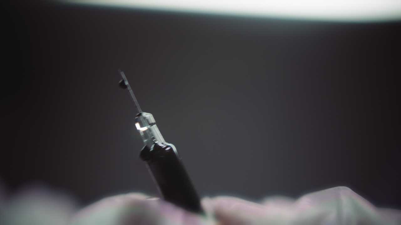 Gloved hands prepare the syringe for injection