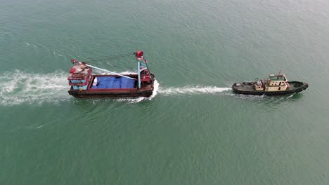 remolcador tirando de una pequeña barcaza en la bahía de hong kong, vista aérea