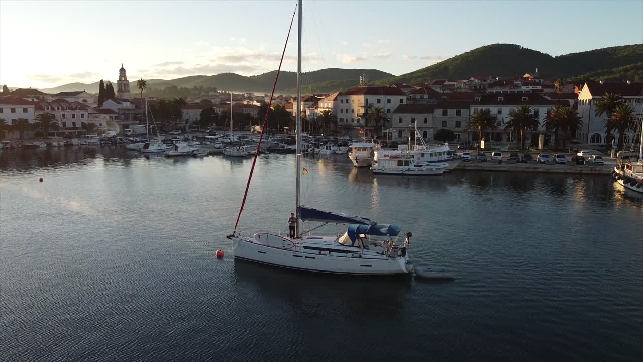 Drone che esegue un movimento di volo a elica attorno a uno yacht ancorato nel porto di un'isola croata.