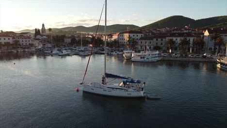 drone doing a helix flight movement around a yacht anchored in the harbour of a croatian island port