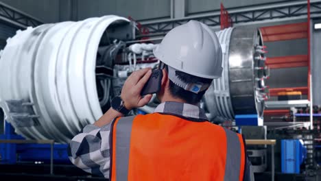 close up back view of asian male engineer with safety helmet talking on smartphone while standing with airplane engine maintenance conducted, analytics checking the turbine