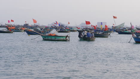 dolly shot of fishermen navigating through the docked sailboats with flags in da nang