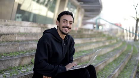 hombre usando una computadora portátil y sonriendo a la cámara