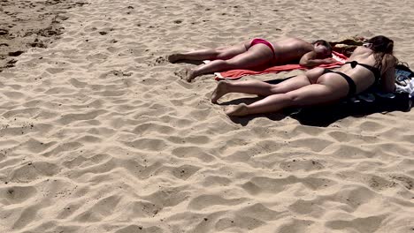 Two-girls-on-the-beach-lying-down-on-the-ground-and-enjoying-warm-sunlight-enjoying-the-sun