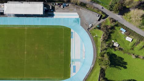 Rising-shot-of-sports-stadium-not-in-use-showing-field,-track-and-grandstand-on-bright-sunny-day