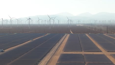 Campo-Solar-De-Paneles,-Gran-Cantidad-De-Turbinas-Eólicas,-Antena-En-Un-Día-Nublado-En-Mojave