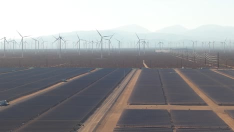 Solar-field-of-panels,-massive-amount-of-wind-turbines,-aerial-on-cloudy-day-in-Mojave