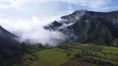 aerial drone dolly-in of fog rolling into a volcanic crater farmland in ecuador