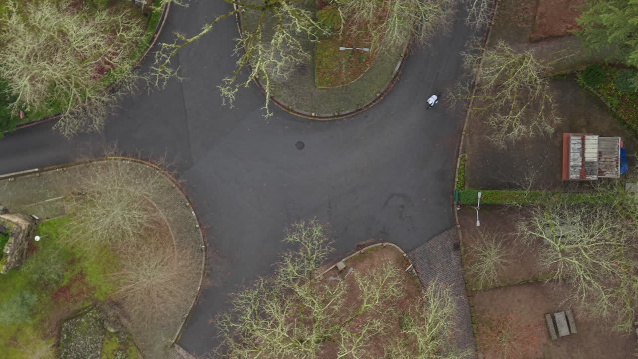 Aerial top view lowering toward cyclist riding on quiet park roads