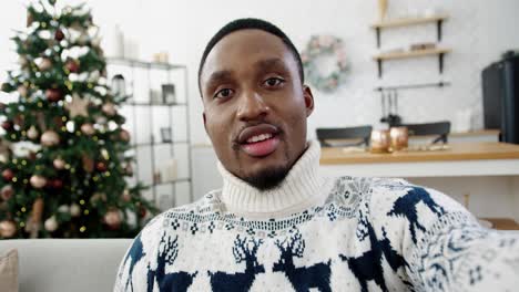 Pov-Of-Happy-Handsome-Male-In-Xmas-Sweater-Videochatting-While-Sitting-Near-Decorated-New-Year-Tree-At-Home